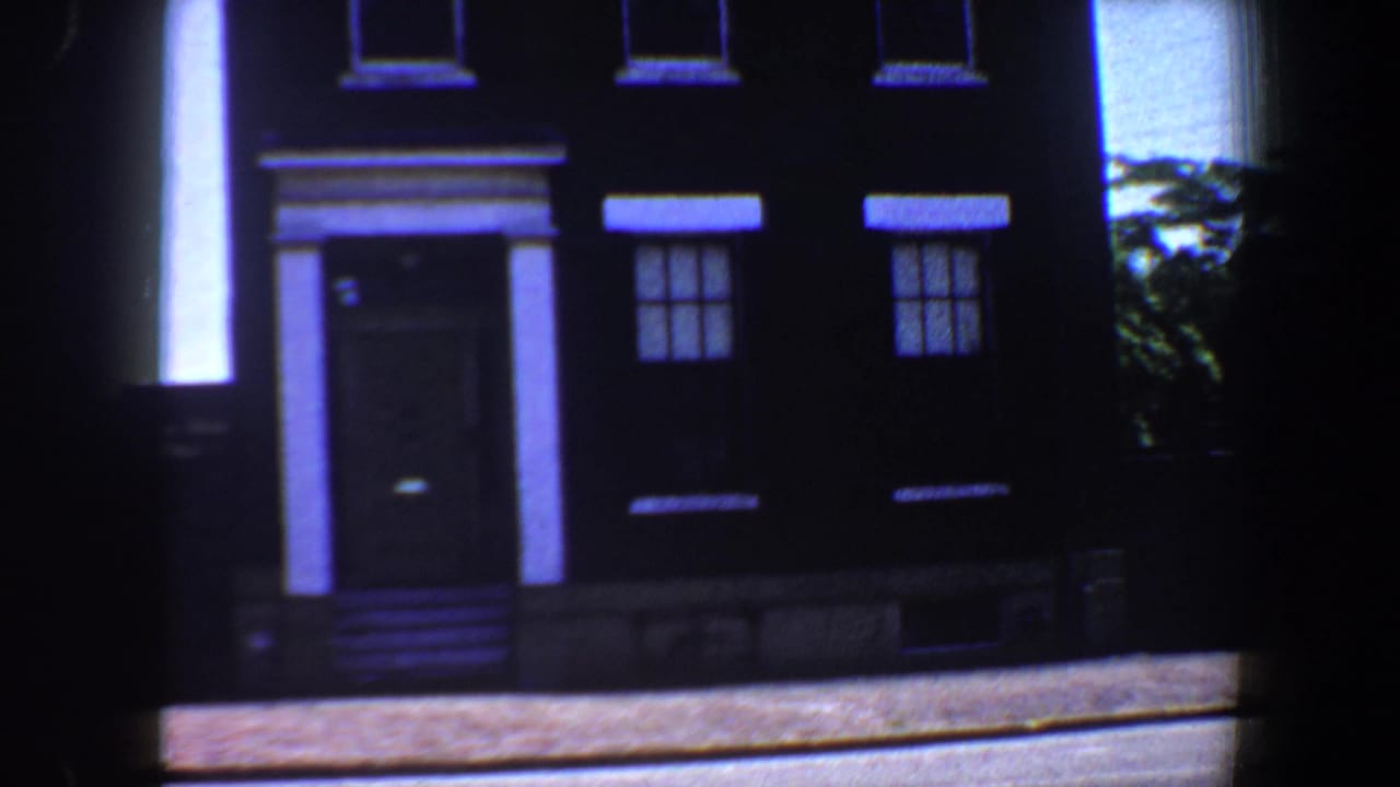 Three-story residential facade with white side trim, doorway, lower windows, steps, and bright street edge.