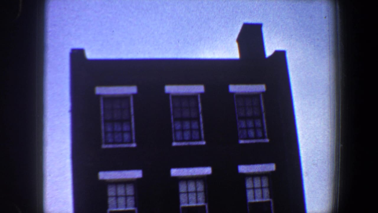 Dark brick building facade with white-trimmed windows against bright sky.