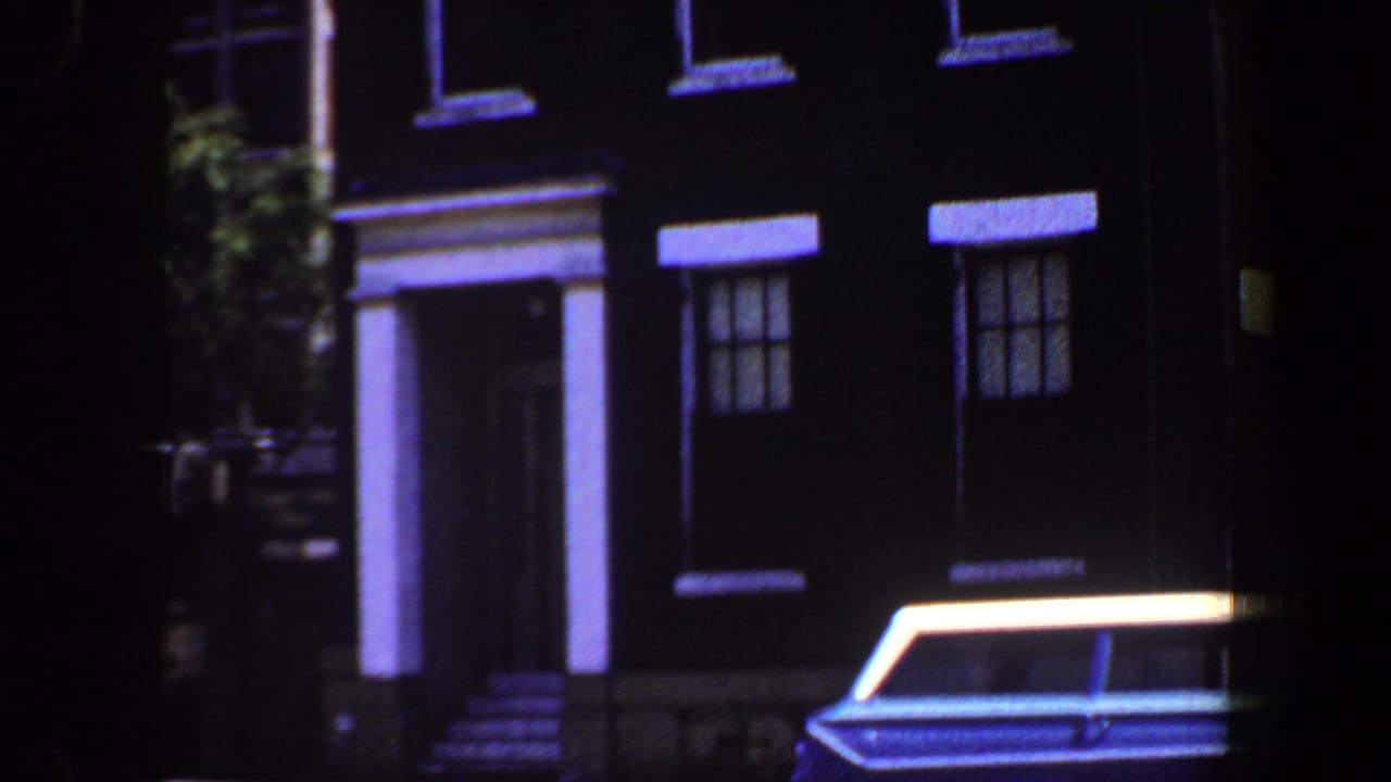 Columned building entrance with a blue-and-white station wagon parked at curb.