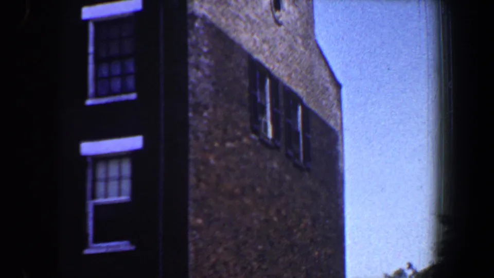 1964 Saint Louis home-movie frame showing a narrow brick side wall, part of the facade, and open sky.