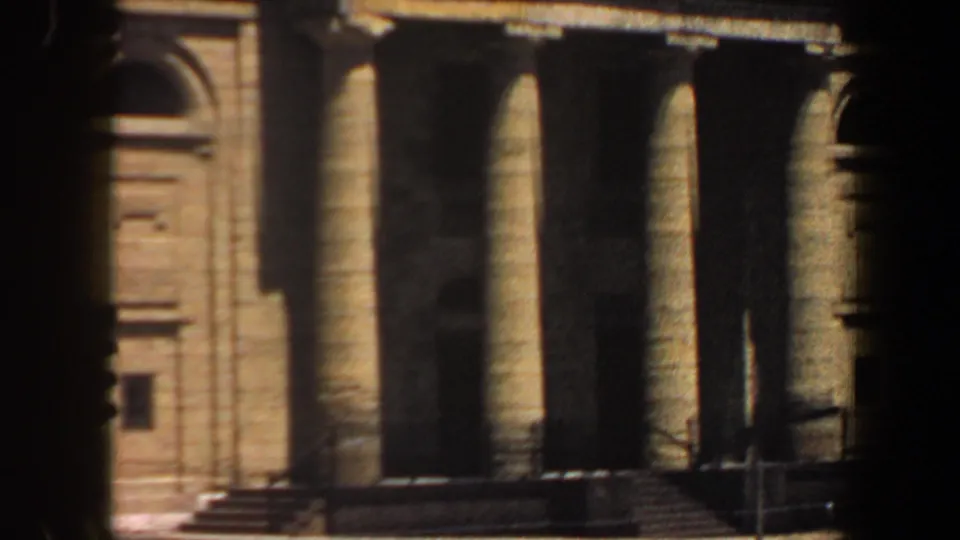 1964 Saint Louis frame of a tan classical-style building with tall columns, steps, and deep portico shadows.