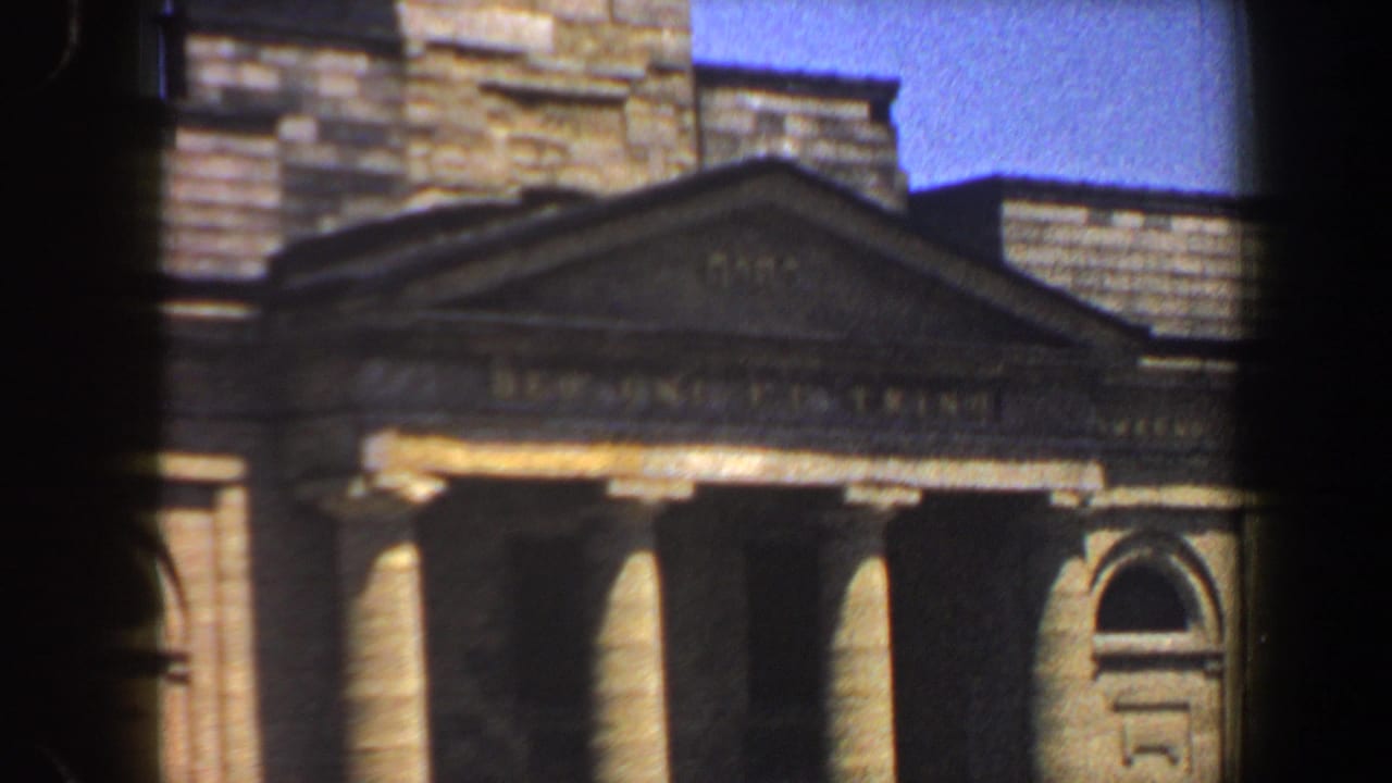 Stone portico, arched window, and roofline seen through a dark film edge.