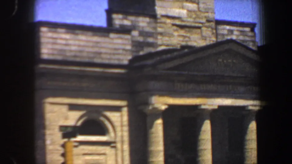 Handheld 8mm frame of the St. Louis building facade, showing arched window detail, columns, pediment, and masonry tower.