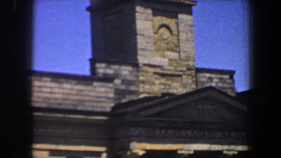 The 1964 home-movie shot frames the masonry tower, triangular pediment, column tops, and clear blue sky in St. Louis.