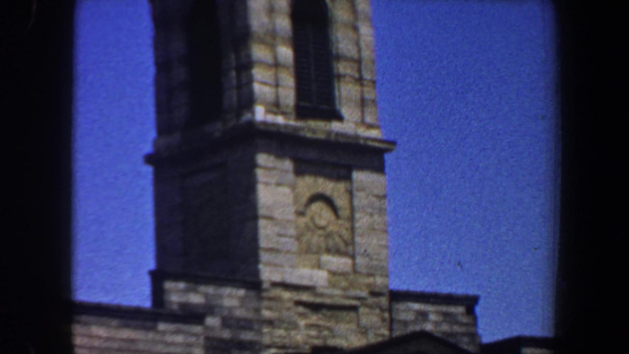 Upper stone church tower with a carved eye-like detail against blue sky.