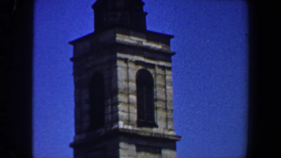 1964 8mm frame showing a church tower belfry with an arched window and the lower part of a pointed steeple.