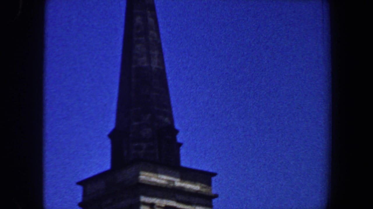 1964 Saint Louis home-movie frame showing the upper portion of a church steeple against a saturated blue sky.