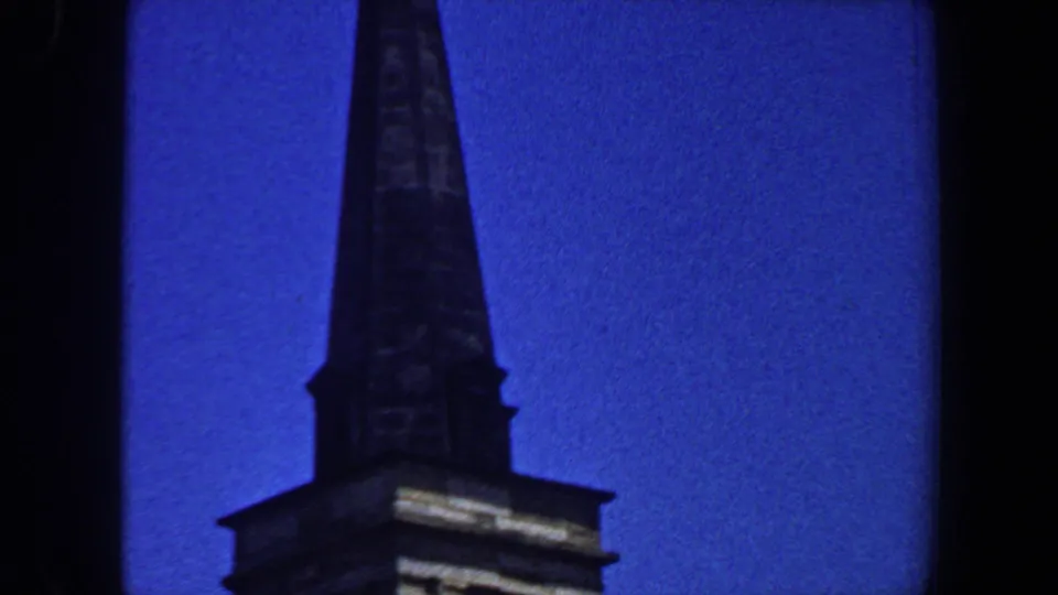 1964 Saint Louis home-movie frame showing the upper portion of a church steeple against a saturated blue sky.