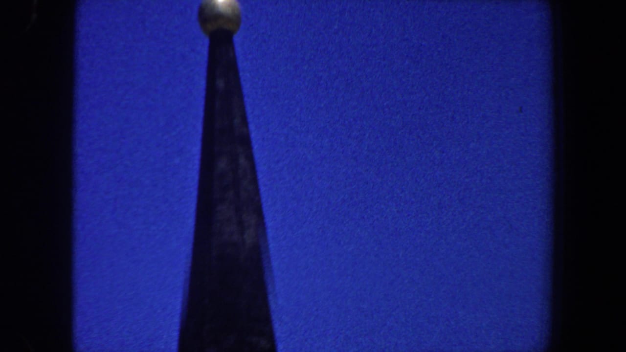 Pointed steeple with a gold-colored orb at the top against blue sky.