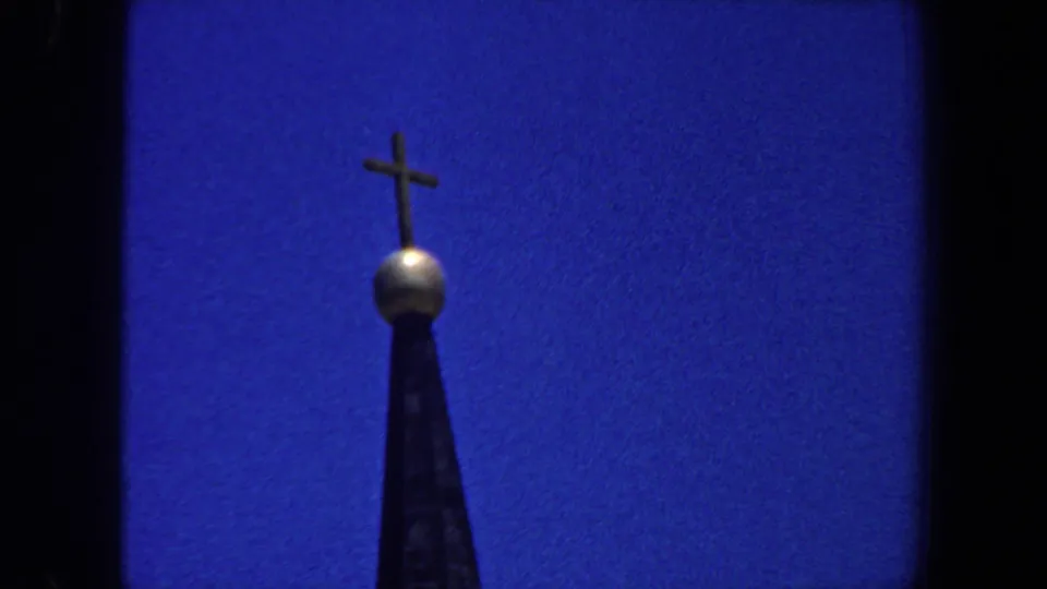 1964 Saint Louis 8mm frame showing the church steeple top, gold-colored orb, and cross against a clear blue sky.