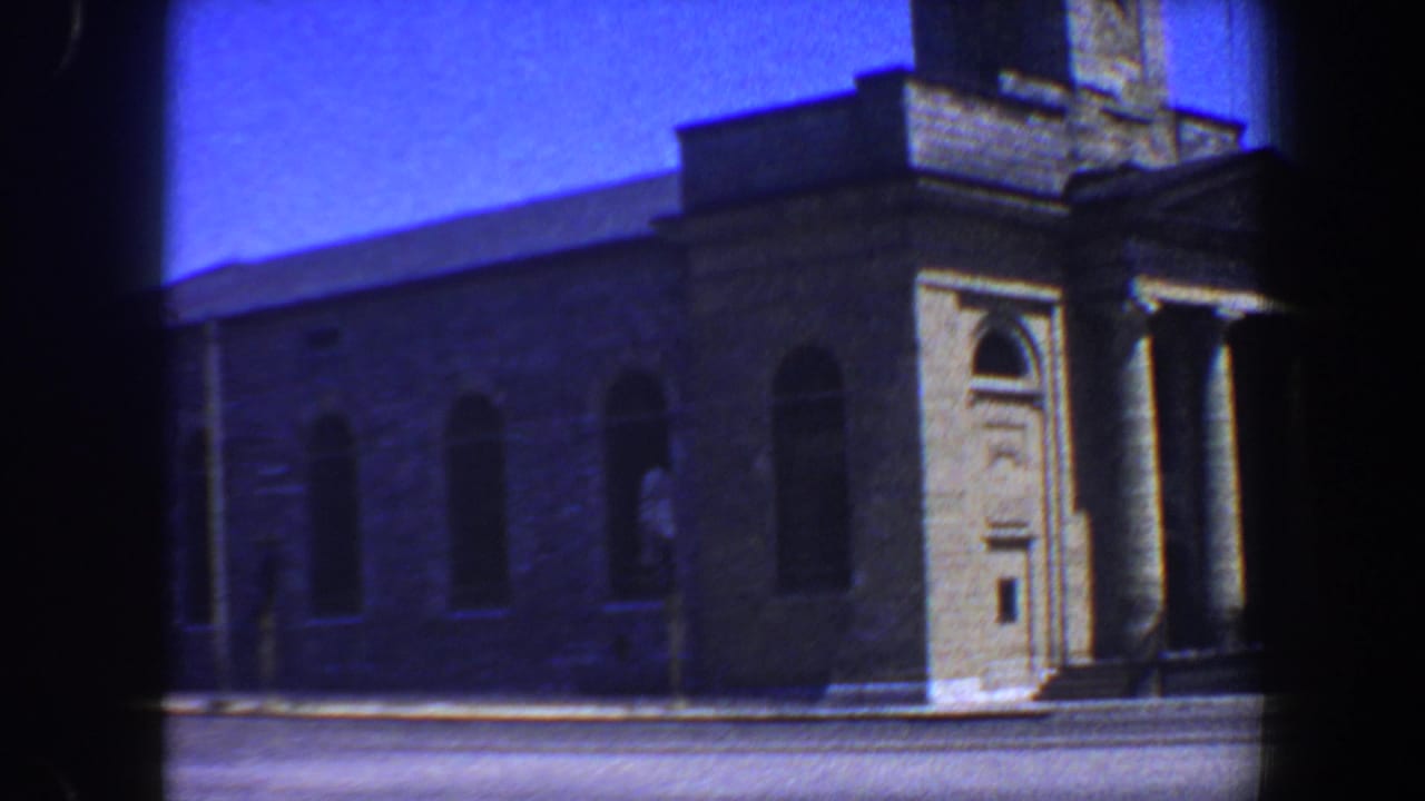 Angled view of a stone building corner with arched windows and a columned doorway.
