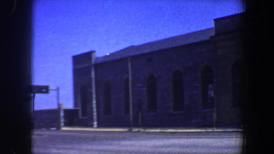 1964 Saint Louis 8mm frame with the building side receding across the street, arched windows visible beneath a blue sky.