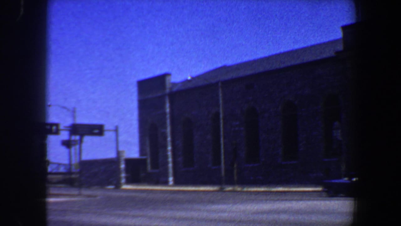 Brick building beside a street with traffic signals and a dark film-edge vignette.