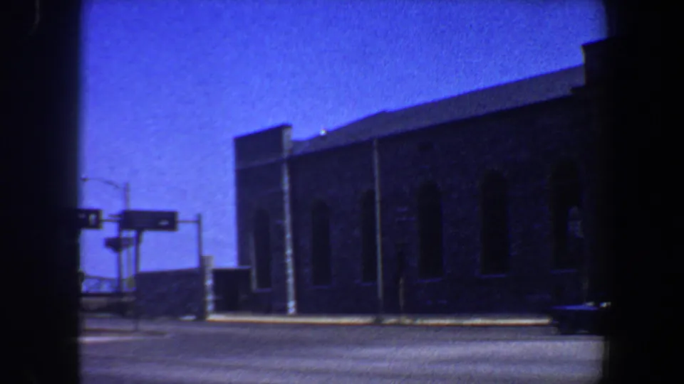 1964 Saint Louis street view with a large brick building, overhead traffic lights, blue sky, and a car near the curb.
