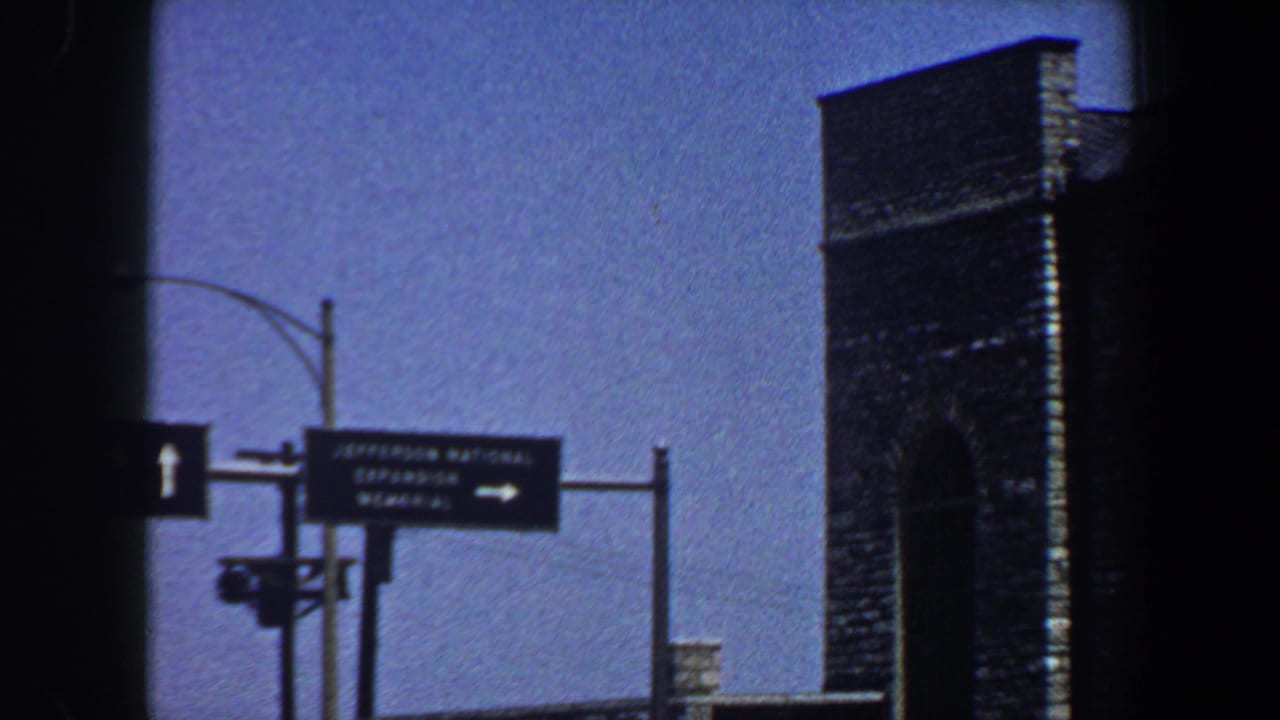 Overhead directional sign near a tall brick or stone structure against blue sky.