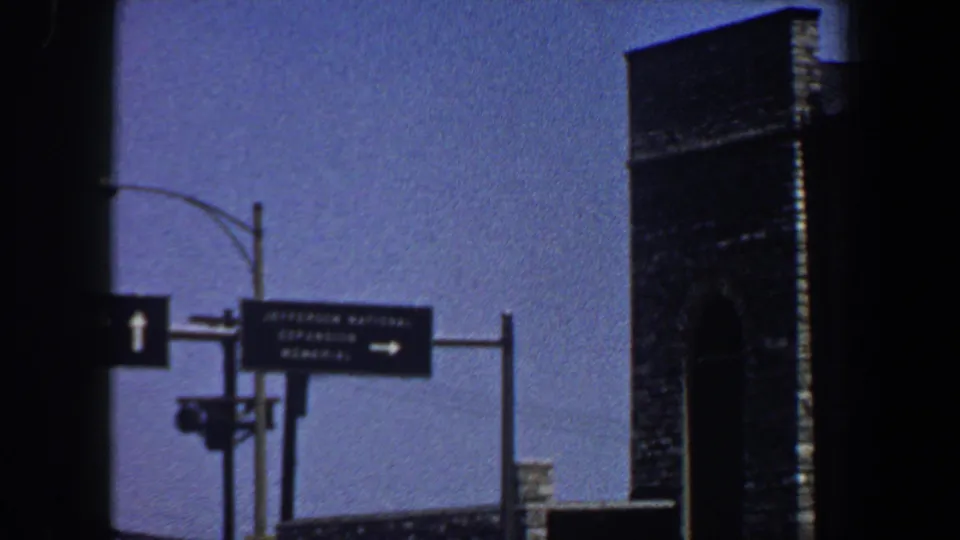 1964 Saint Louis traffic-control view with directional arrows, a Jefferson National Expansion Memorial sign, and a tall masonry structure.
