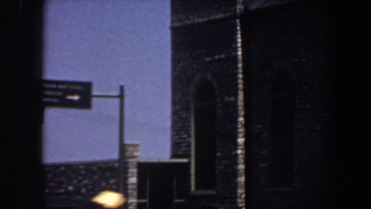 Directional street sign beside a dark brick building with arched openings.
