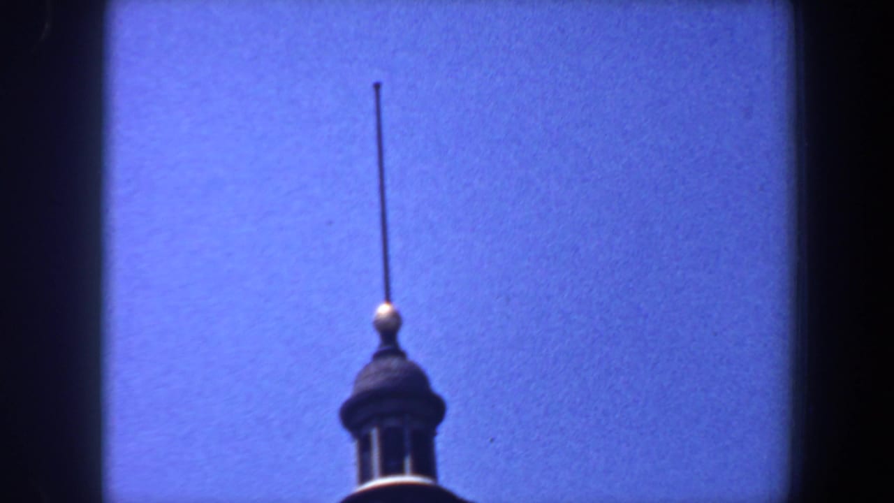 Upper cupola and tall spire silhouetted against a blue sky.