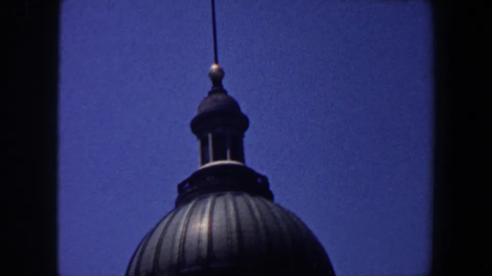 Close 1964 Saint Louis 8mm view of a dark domed roof with cupola and spire against a grainy blue sky.