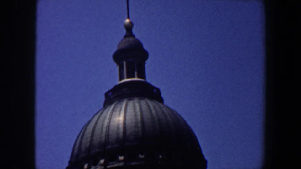 1964 Saint Louis home-movie frame showing the upper dome, lantern, and spire of a historic-looking building against blue sky.