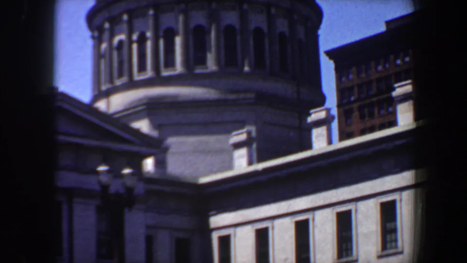 A handheld 8mm view shows the domed Saint Louis building with arched windows, a streetlamp, and surrounding urban architecture.