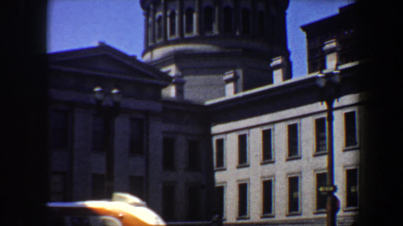 Grey stone building with domed tower as a light-colored car crosses the lower frame.