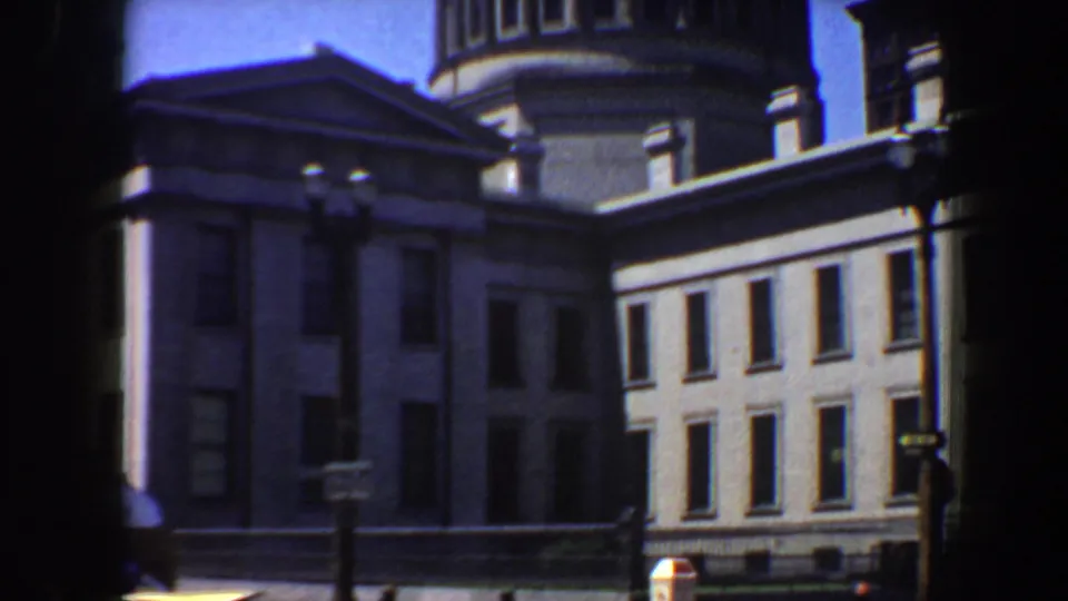1964 Saint Louis footage frames the grey classical facade, tower, street lamps, and signs from across the street.