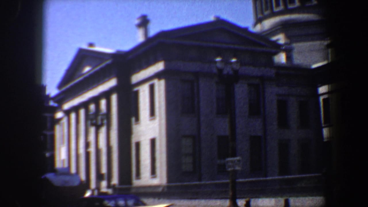 1964 Saint Louis 8mm frame showing a columned classical building under blue sky, partly obscured by dark foreground edges.