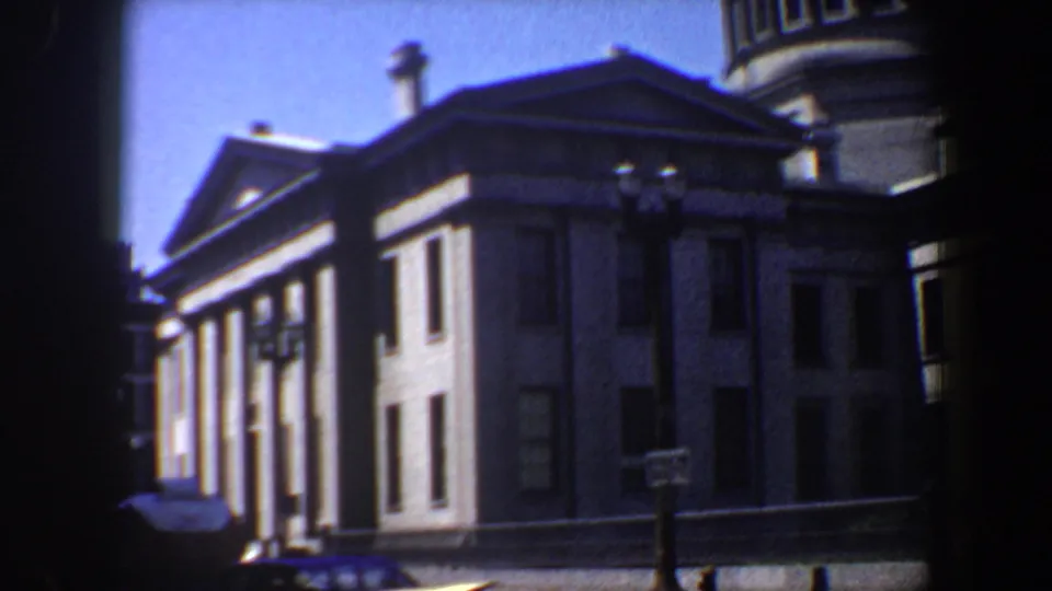 1964 Saint Louis 8mm frame showing a columned classical building under blue sky, partly obscured by dark foreground edges.
