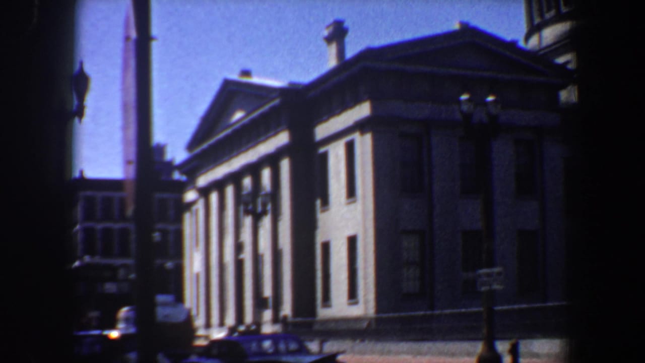 Columned building facade with pediment, street lamp, and curbside car below.