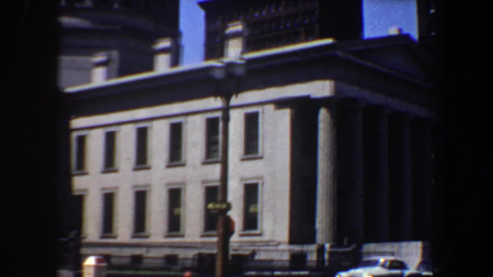 Saint Louis 1964 frame showing the building's windowed side, street lamp, dark foreground edge, and a small car at lower right.