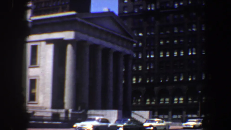 1964 Saint Louis exterior view showing the columned facade, pediment, office towers behind it, and cars at street level.