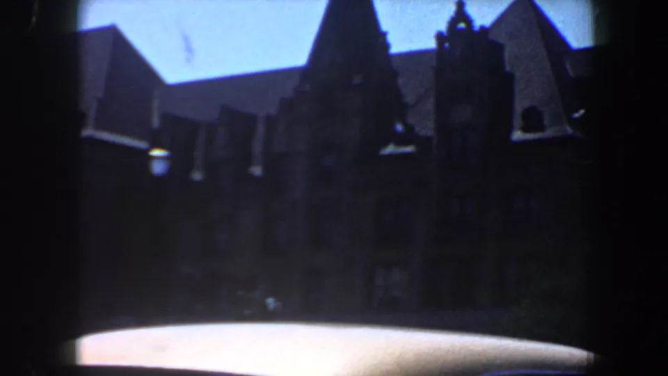 Soft 8mm frame of a large historic Saint Louis building with steep roof peaks, dark windows, blue sky, and car roof foreground.