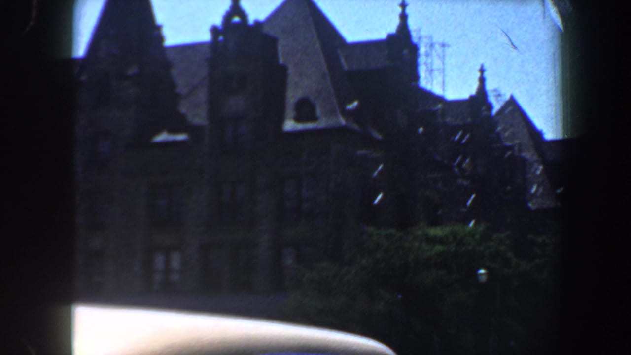 Ornate stone building with spires partly hidden by trees and a car roof.