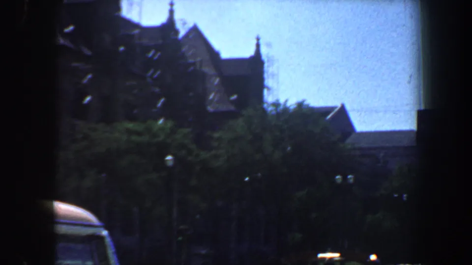 1964 St. Louis street footage with ornate architecture receding behind trees and a partial car visible at the lower left.