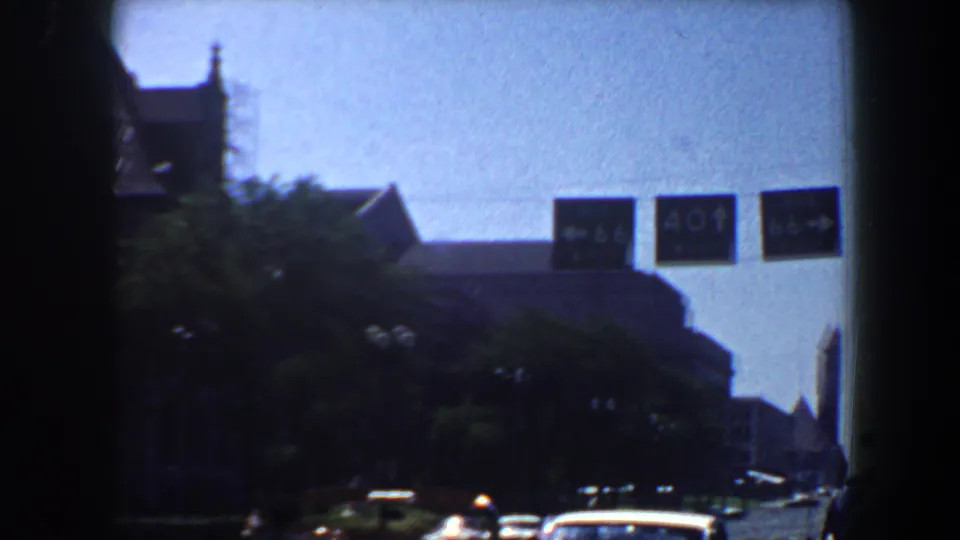 1964 Saint Louis roadway frame showing traffic, trees, and visible I-64 and I-40 route signs beside older architecture.