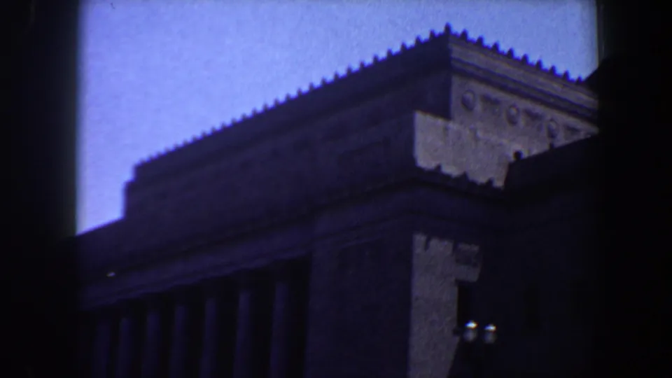 Large classical-style building in Saint Louis, filmed from the street with columns, stone facade, and serrated roofline visible.