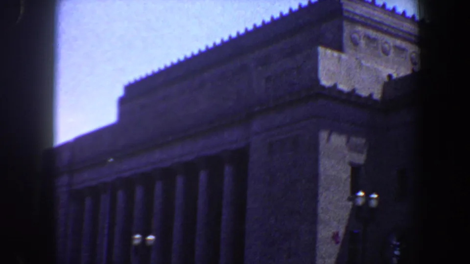 Street-level 1964 Saint Louis view of a large columned building with decorative roofline and lamps in the foreground.