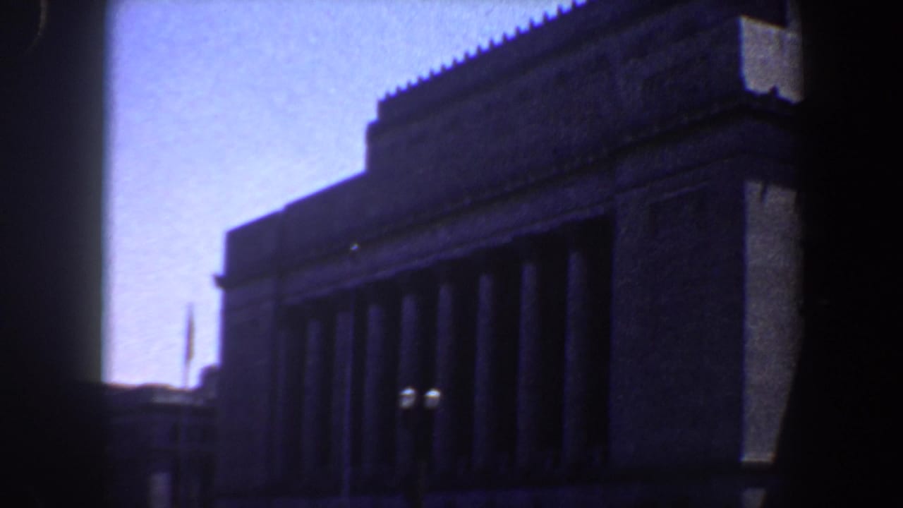 1964 Saint Louis home-movie frame of a large columned building facade with streetlamps and traffic below.