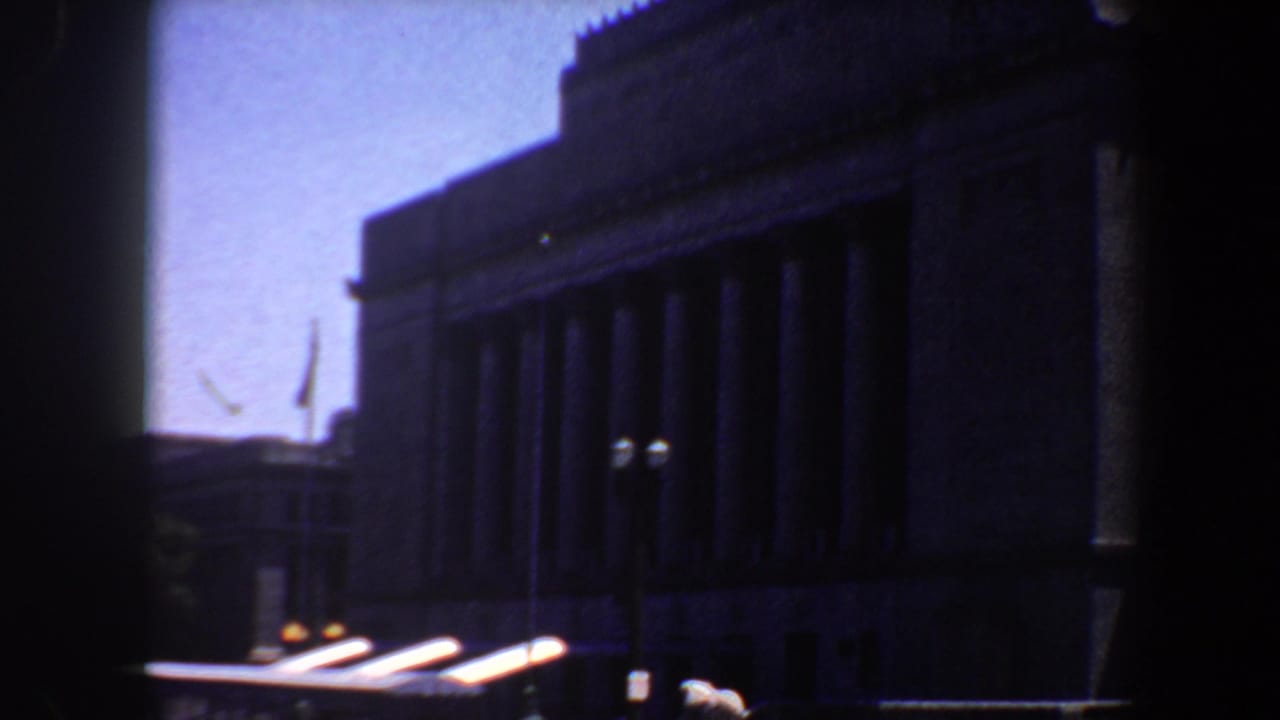 Columned building with a bright car roof passing along the street below.