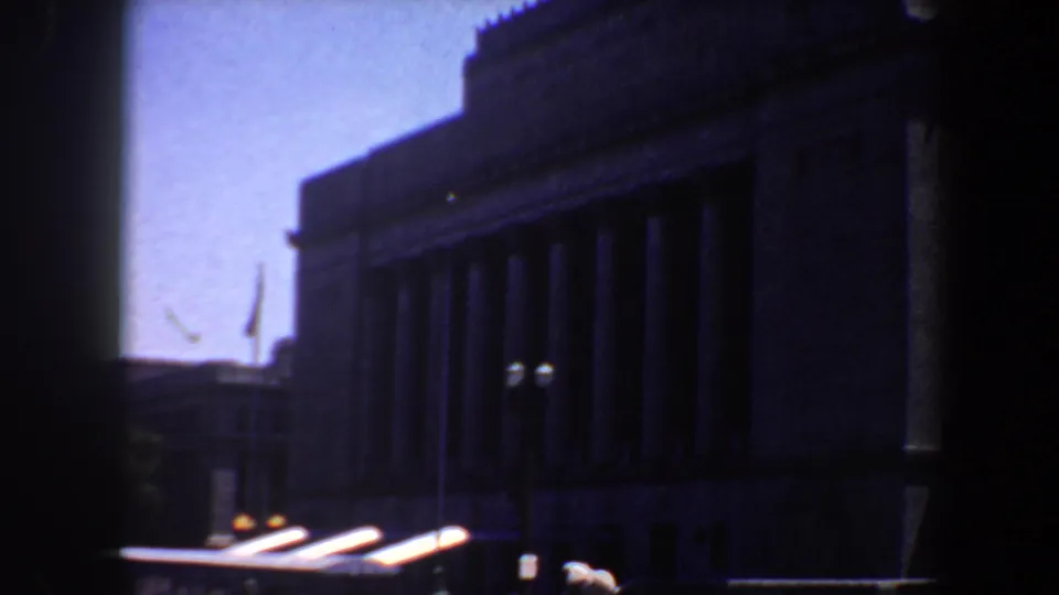 A dark columned facade in Saint Louis with sunlit car surfaces moving through the lower edge of the 8mm frame.