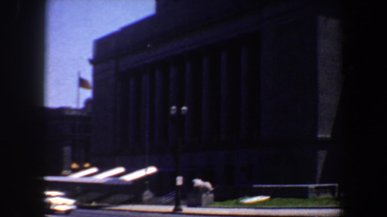 1964 St. Louis library exterior with stone columns, flag, streetlamps, and dark window-frame bars in the foreground.