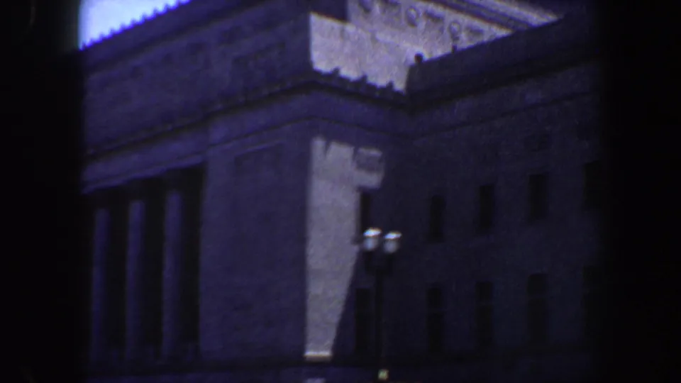 Close, soft 8mm view of the St. Louis library facade, with roofline detail, shadowed columns, and a streetlamp in front.