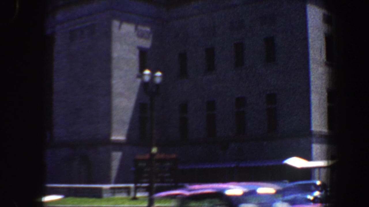 1964 Saint Louis street view of a large institutional-looking building with rectangular windows, lamps, signage, and passing cars.