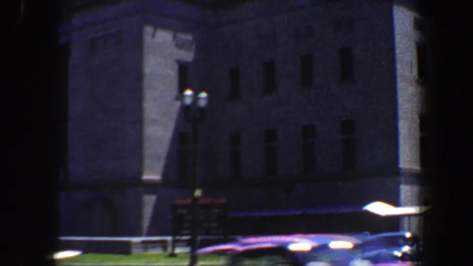 1964 Saint Louis street view of a large institutional-looking building with rectangular windows, lamps, signage, and passing cars.