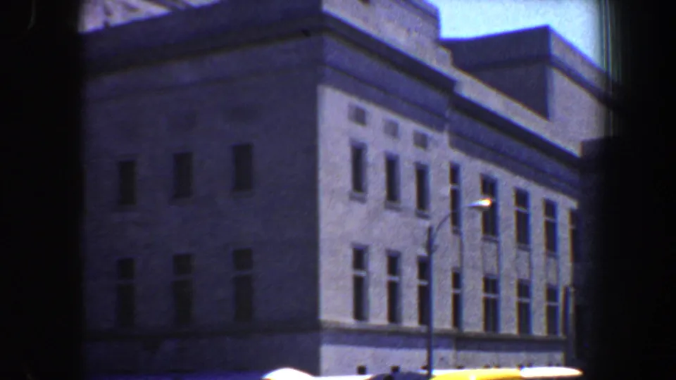 1964 Saint Louis frame showing the upper stories of a large institutional-style building, with window rows and streetlamps in front.