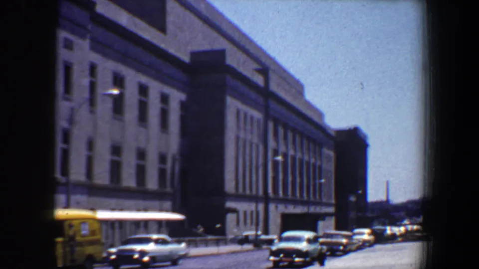 Saint Louis street traffic in 1964, with a yellow van or bus near a large civic-style facade.