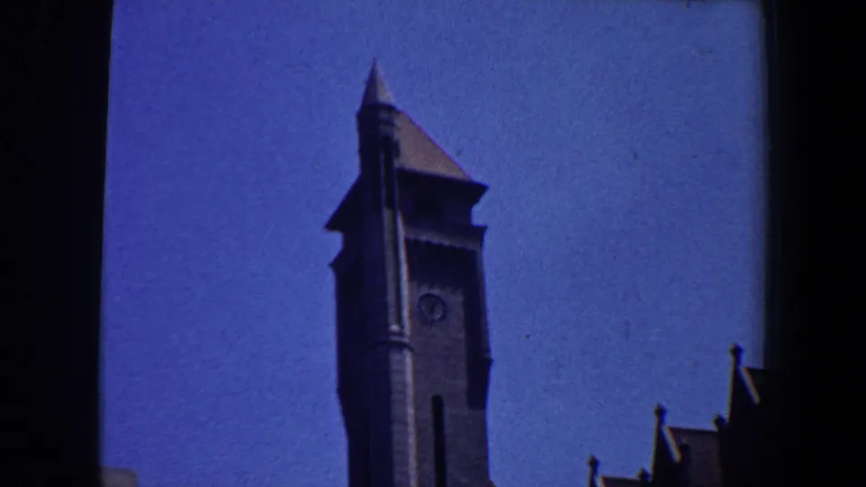 1964 Saint Louis view of a tall clock tower and nearby steep rooflines under a deep blue sky.