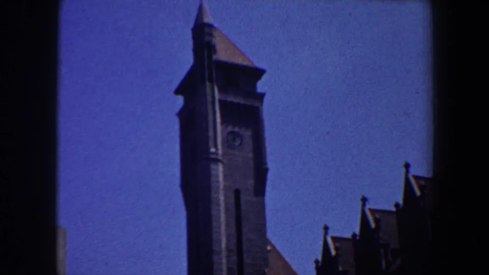 Saint Louis clock tower detail from 1964 home-movie footage, framed with roof peaks and open sky.