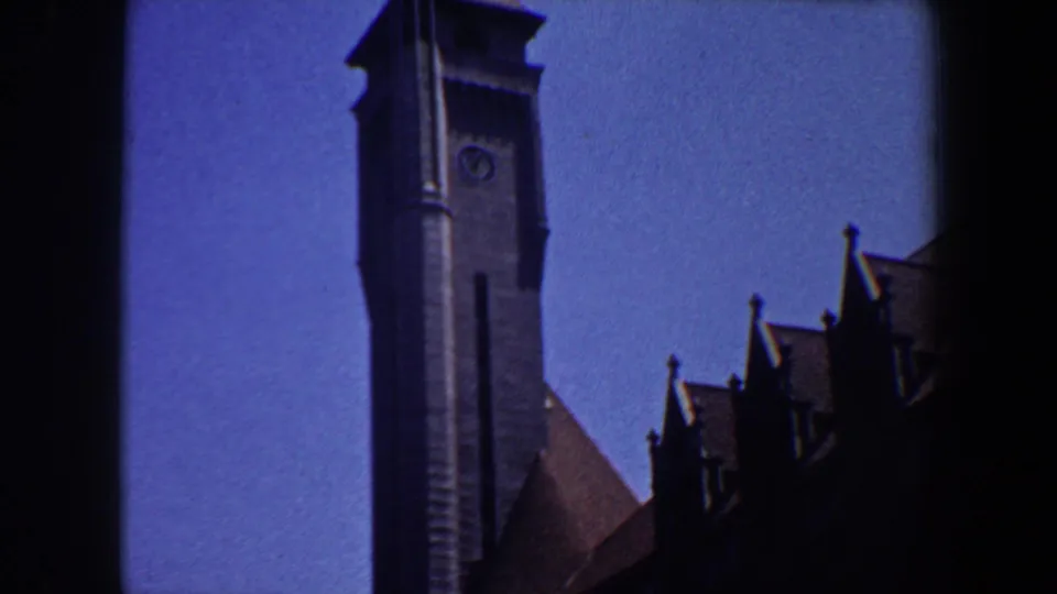 1964 Saint Louis 8mm frame with a tall grey belltower, clock face, and shadowed roof peaks seen from a low angle.